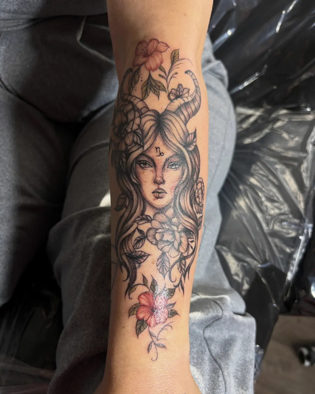 Black and grey portrait of a woman framed by flowers with red accents, on the forearm