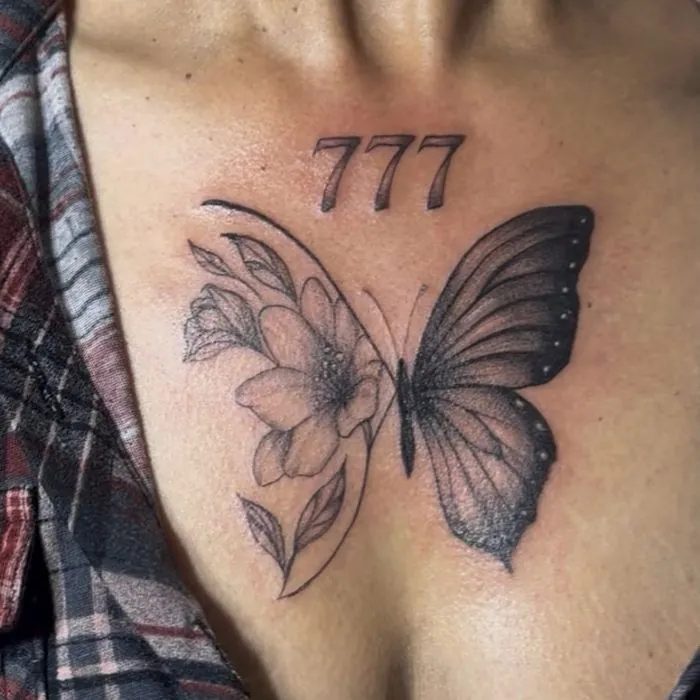 Black and gray butterfly and flower tattoo on the chest beneath the numbers 777. View on Instagram.