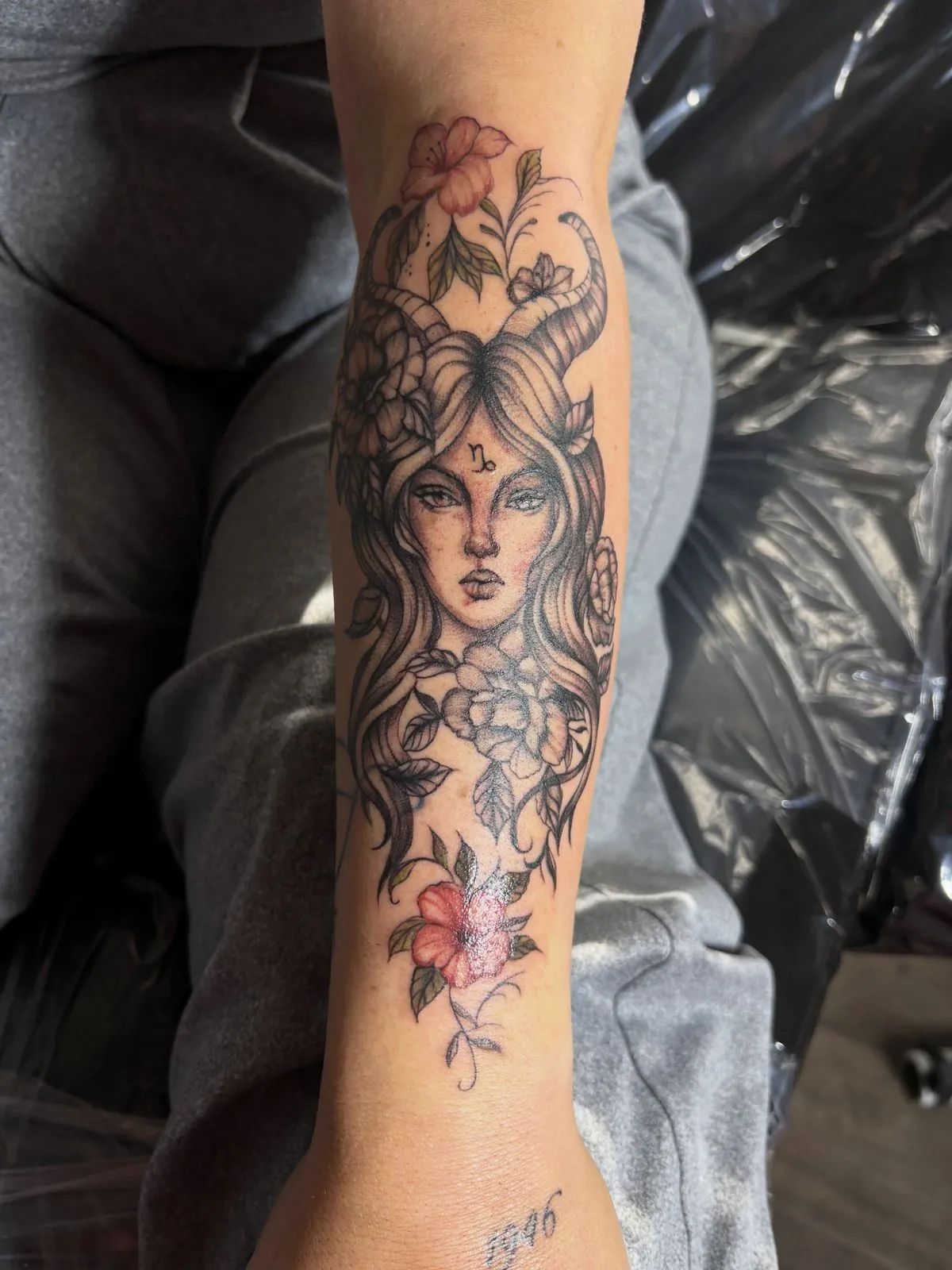 Fine line and black and gray forearm tattoo of a woman's portrait framed by flowers, with red floral accents