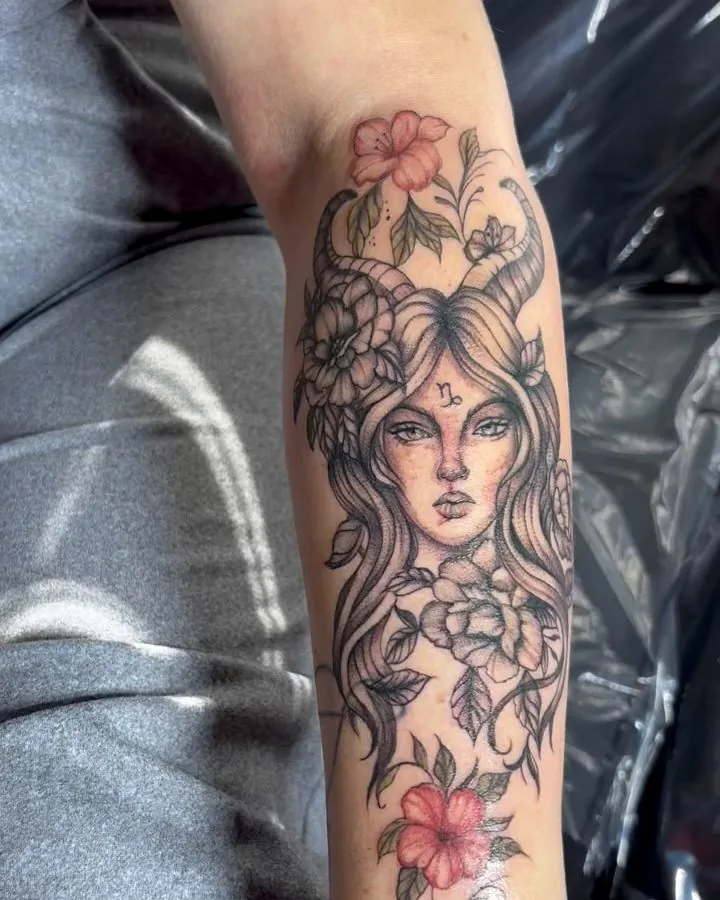 Black and grey forearm portrait tattoo of a woman framed by flowers with red accents